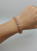 Gold base and pink stone bracelet on a wrist against a plain background