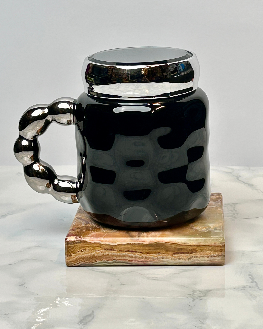 Black mug with silver handle and lid on a marble coaster
