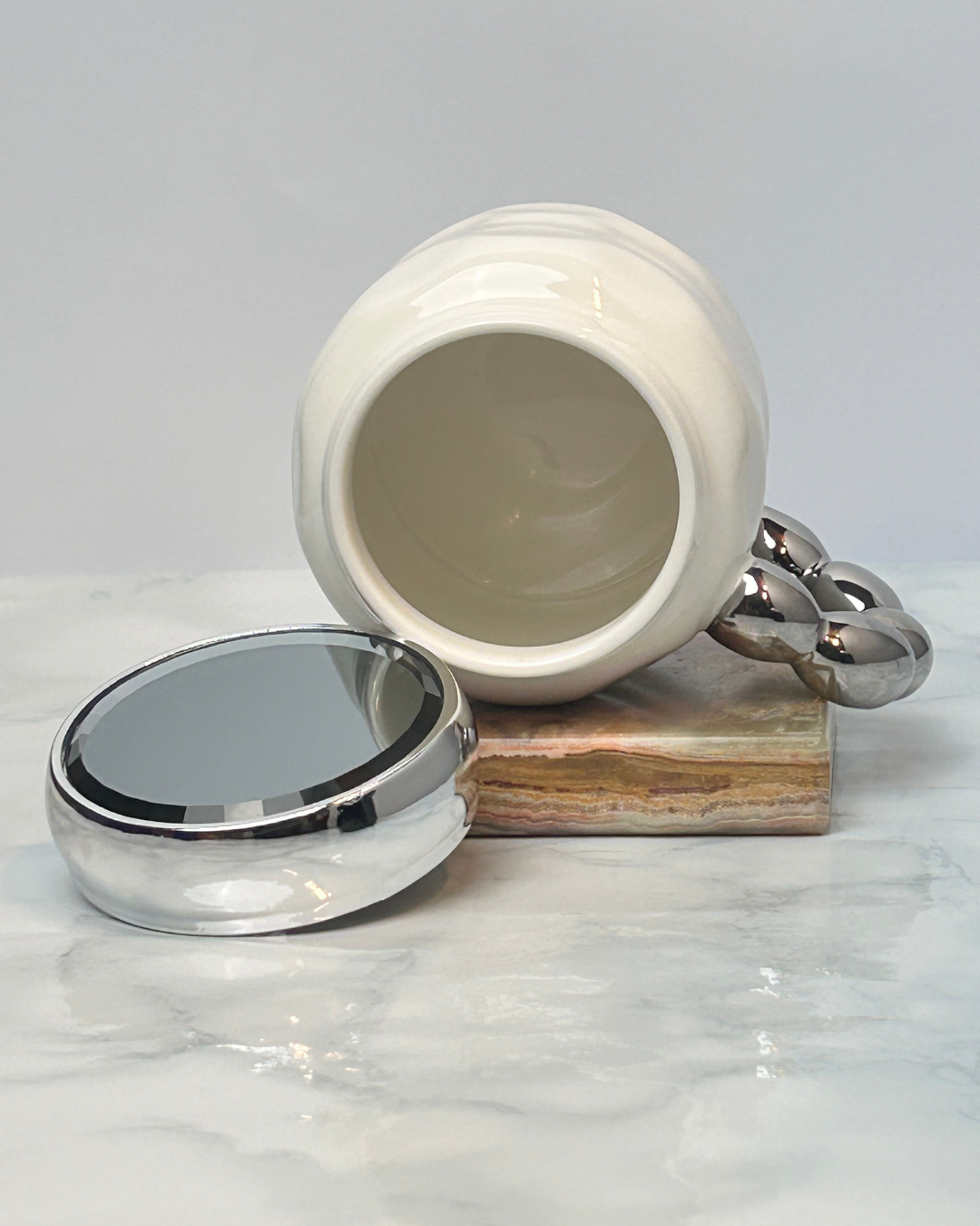 White ceramic jar with silver lid on a marble surface